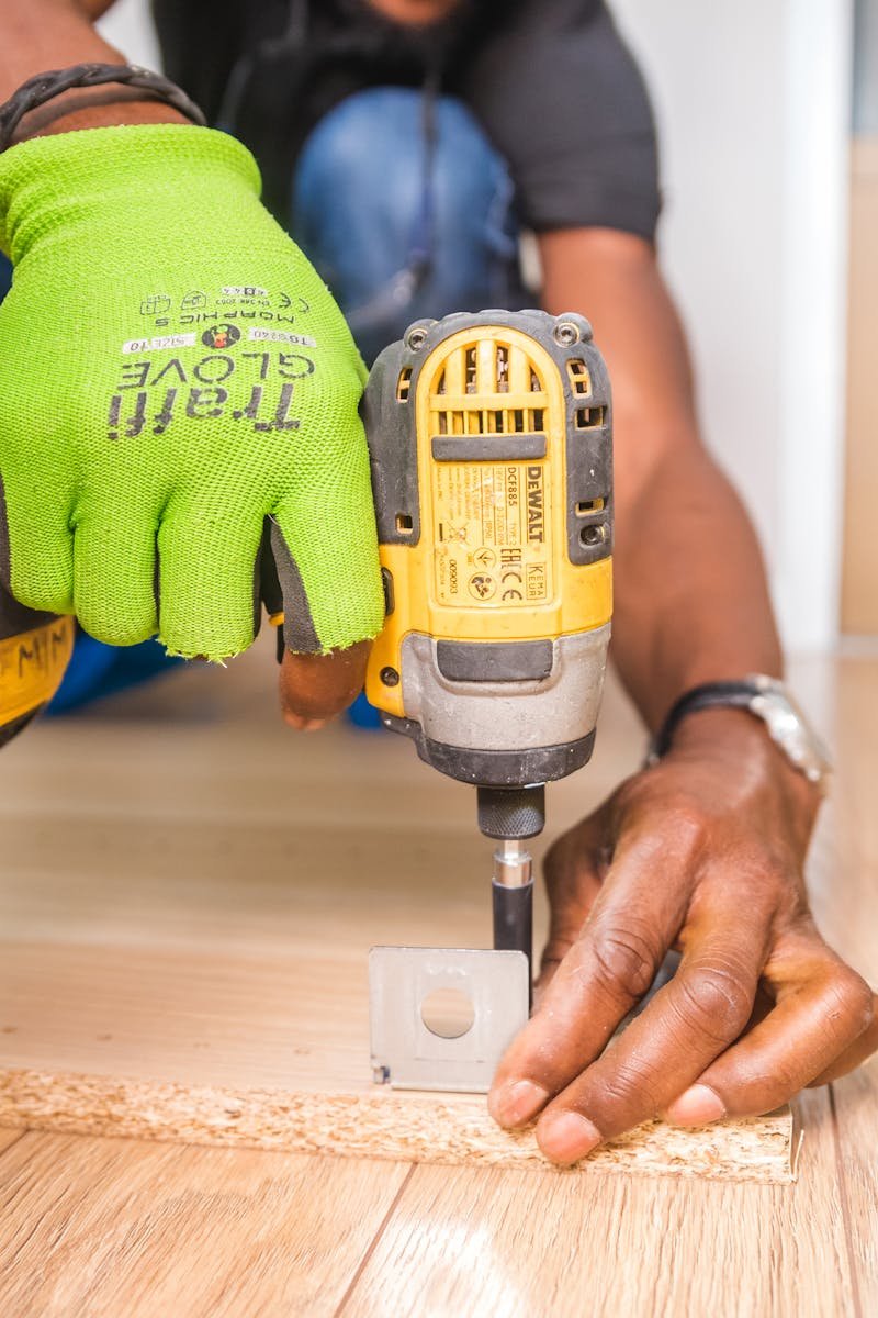 Man using a power drill for home improvement on a wooden floor with precision.