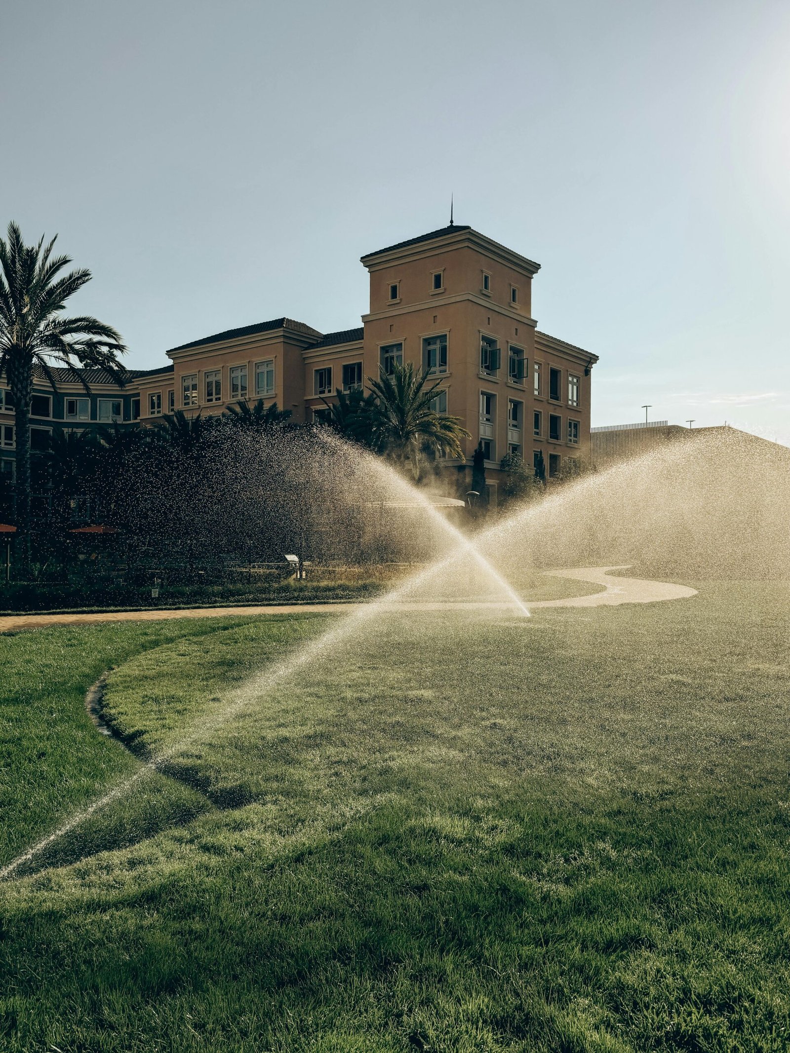 A charming building with a lush green lawn and sprinklers in action under a clear sky in Santa Clara, CA.